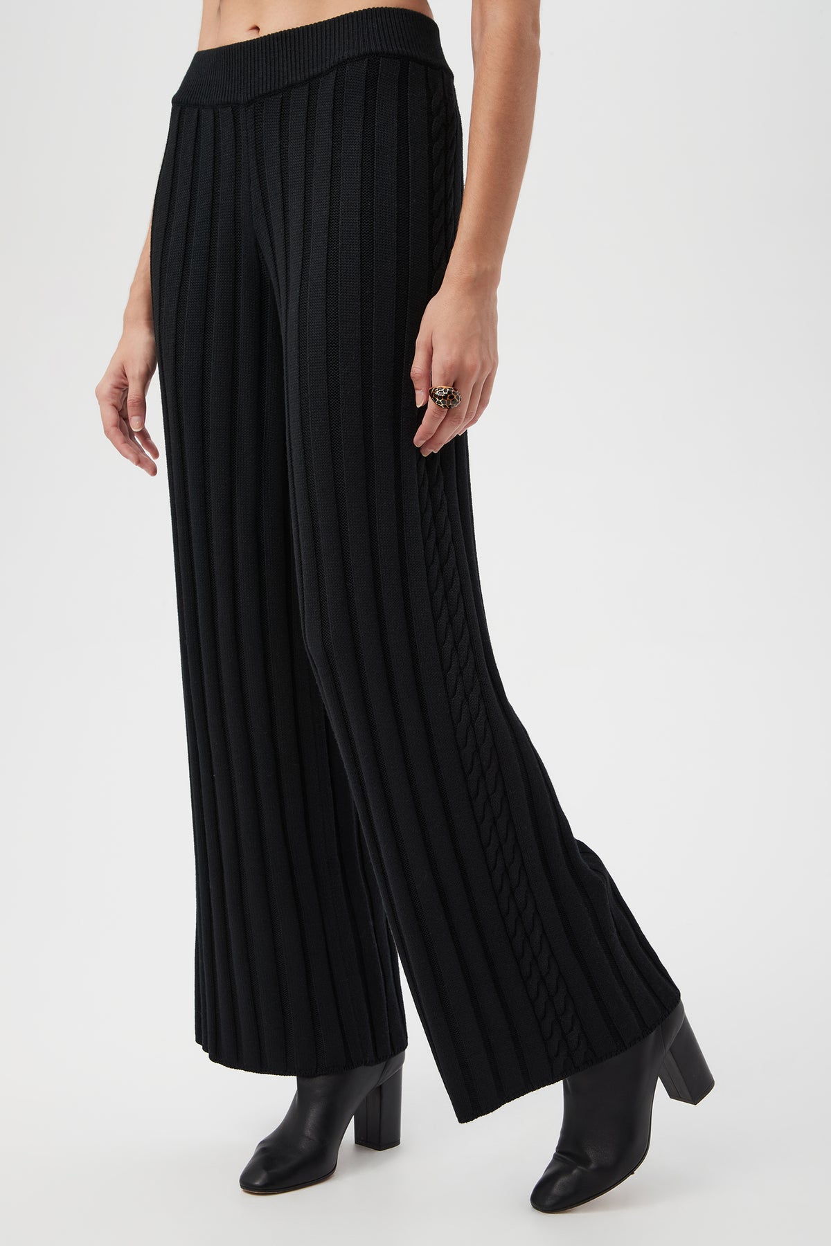 A person wearing the Pearce 2 Pant, which is high-waisted, wide-leg, black ribbed knit with vertical stripes, styled with black heeled ankle boots and a ring on their right hand.