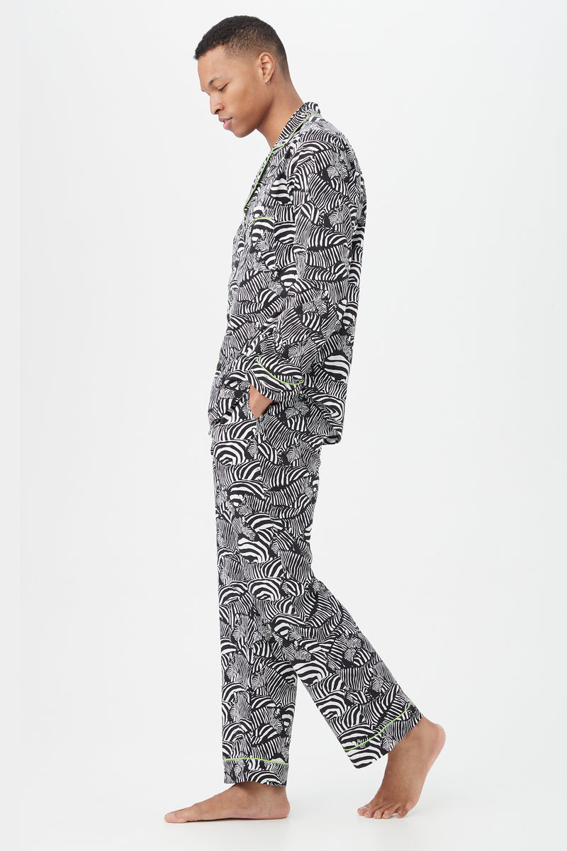 A person stands barefoot in profile against a white background, wearing the Zebra Safari Mens Long Sleeve Long Pant Poplin PJ Set, hands in pockets and looking down to highlight the relaxed style and lightweight feel of these patterned pajamas.