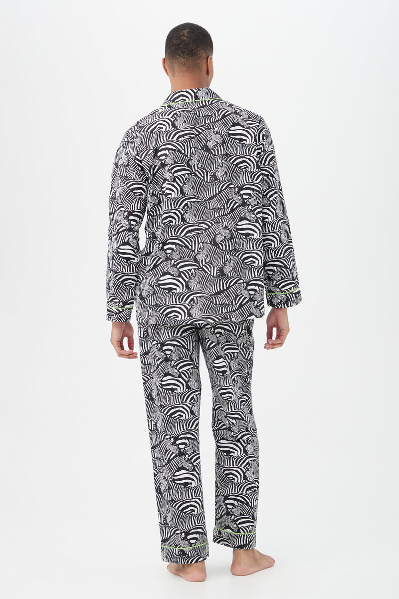A person stands barefoot with their back to the camera, modeling the Zebra Safari Mens Long Sleeve Long Pant Poplin PJ Set with a bold black and white zebra pattern. The lightweight pajamas contrast against a plain white background.