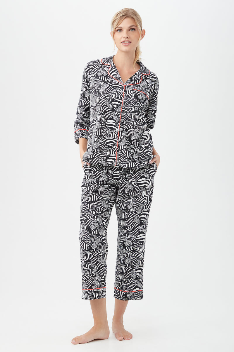 A woman stands barefoot in the Zebra Safari Womens 3/4-Sleeve Cropped Pant Poplin PJ Set in Black/White, hands in pockets against a plain white backgroundâ€”modern, stylish sleepwear for women.