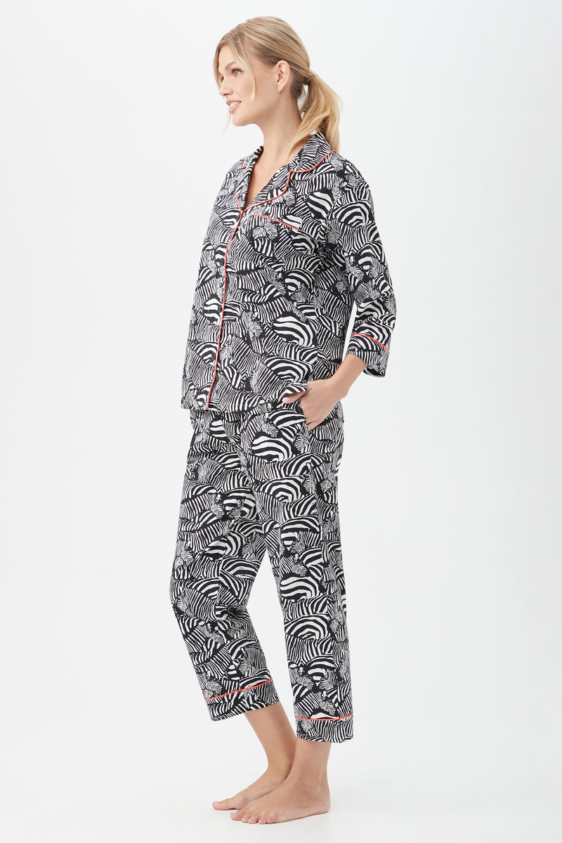 A woman with blonde hair in a low ponytail stands barefoot in profile, smiling softly as she models the Zebra Safari Womens 3/4-Sleeve Cropped Pant Poplin PJ Set against a plain white background.
