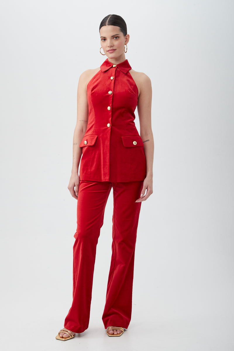 A woman stands against a white background wearing the Elainia Velveteen Sleeveless Tunic Top in red with a collar and matching pants. Her hair is tied back, and she accessorizes with hoop earrings and open-toe sandals.