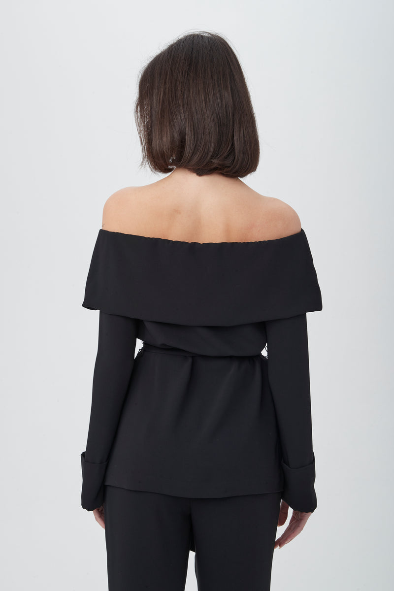 A woman with shoulder-length brown hair, seen from the back, wears the Lyndi Off-The-Shoulder Belted Long Sleeve Top and matching black pants against a plain white background.