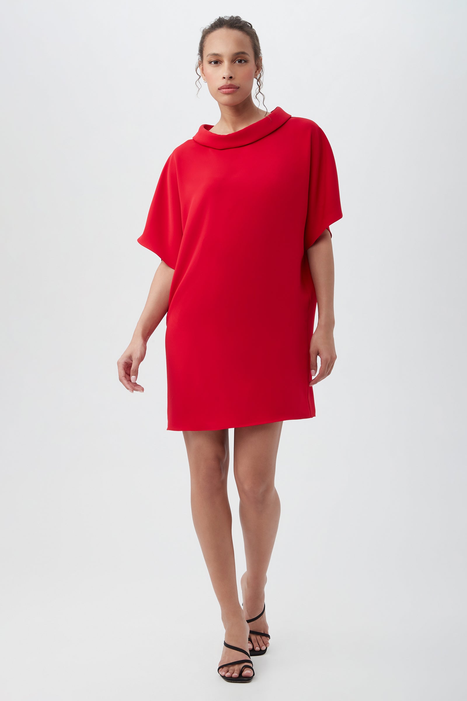 A woman wearing the Honeysuckle Short Dolman Sleeve Shift Dress in Red Spark stands against a plain white background, styled with black heeled sandals.