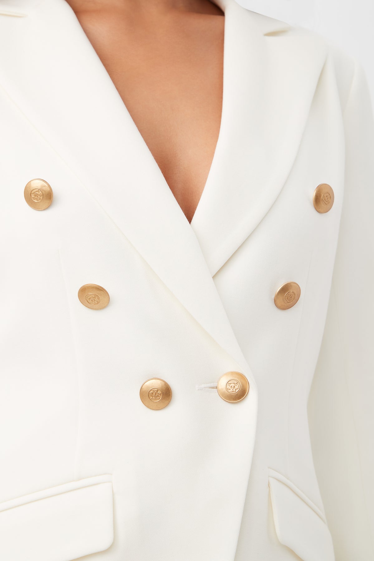 A close-up of a person wearing the Midlands Luxe Drape Stretch Blazer Jacket in white with gold buttons and two front pockets. Only their lower face, neck, and chest are partially visible.