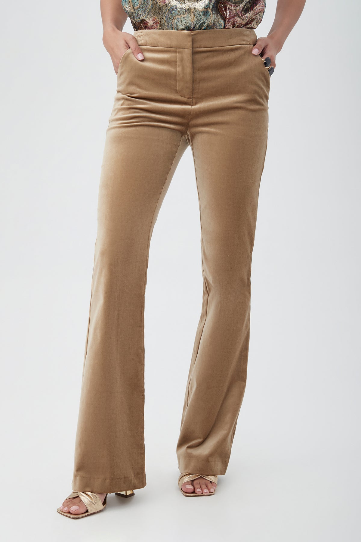 A person wears the Westport Velveteen Bootcut Pant in tan, paired with a patterned tucked-in top and gold open-toe heels, standing against a plain light background.