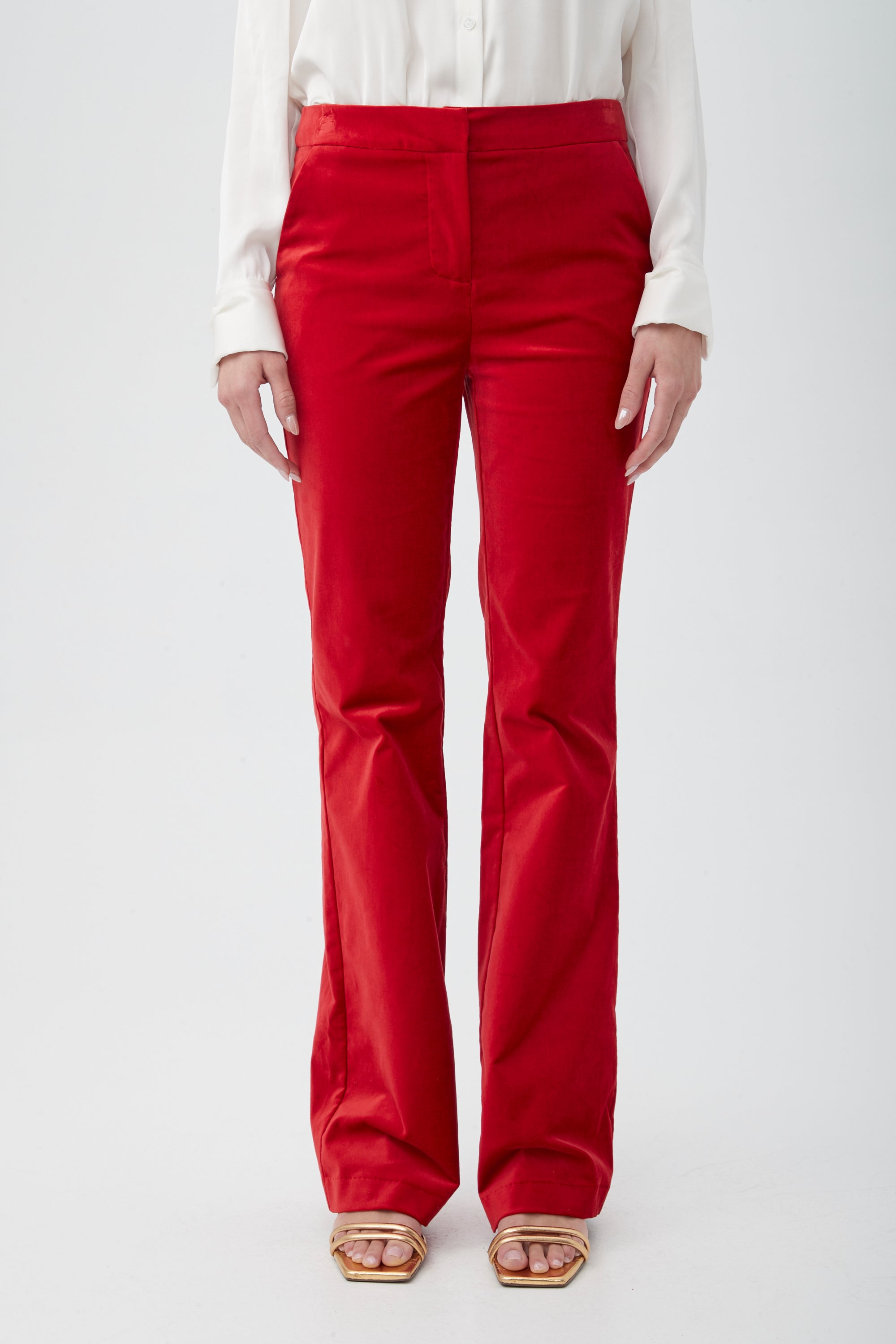 A person wearing the Westport Velveteen Bootcut Pant in bright red, paired with a white long-sleeve shirt and beige open-toe heeled sandals, stands against a plain white background with only the lower half of the body visible.