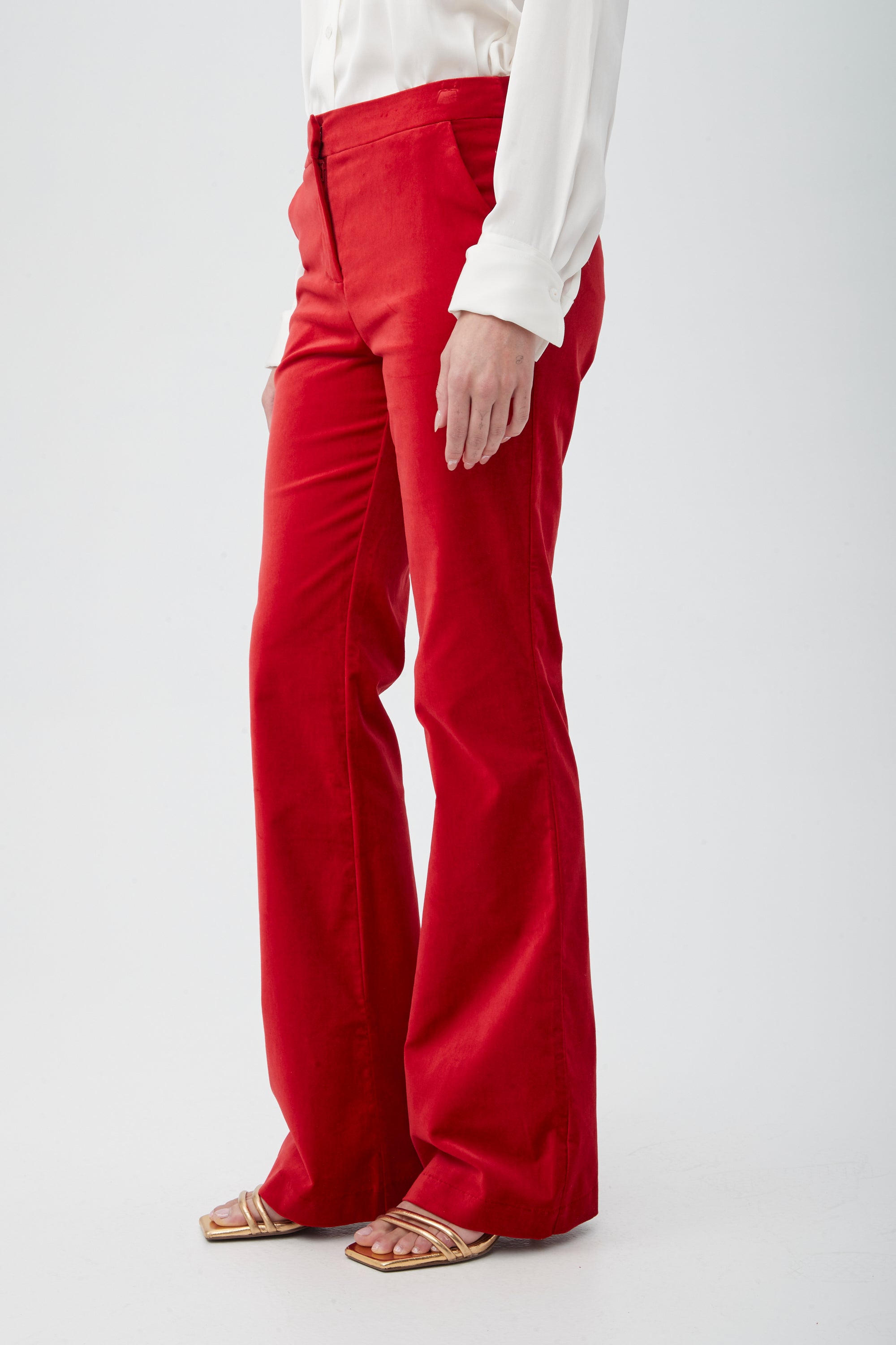 A person models the Westport Velveteen Bootcut Pant in bright red, paired with a white long-sleeve blouse and gold open-toe sandals against a plain white background. Only their lower body is visible.