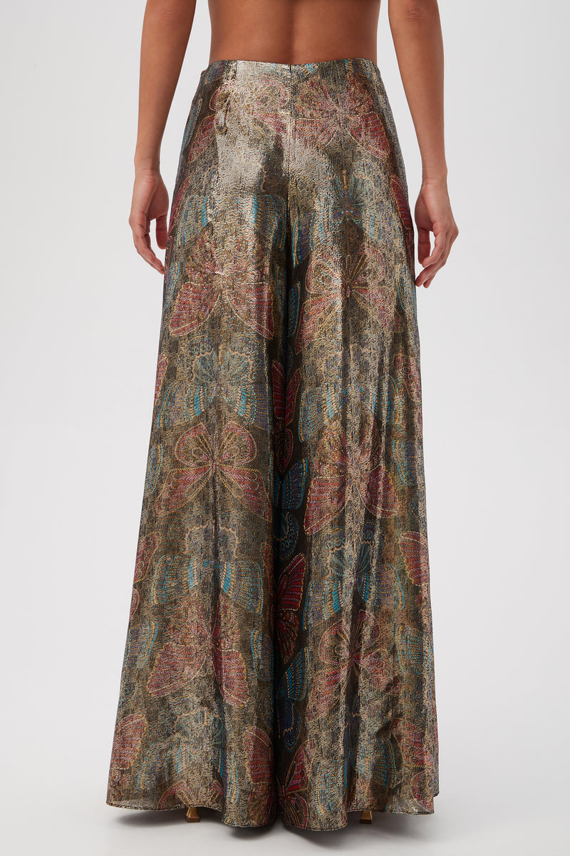 A person wears Siya Butterfly Print Silk Wide Leg Pant in Multi, featuring a metallic-patterned design, barefoot against a plain white background.