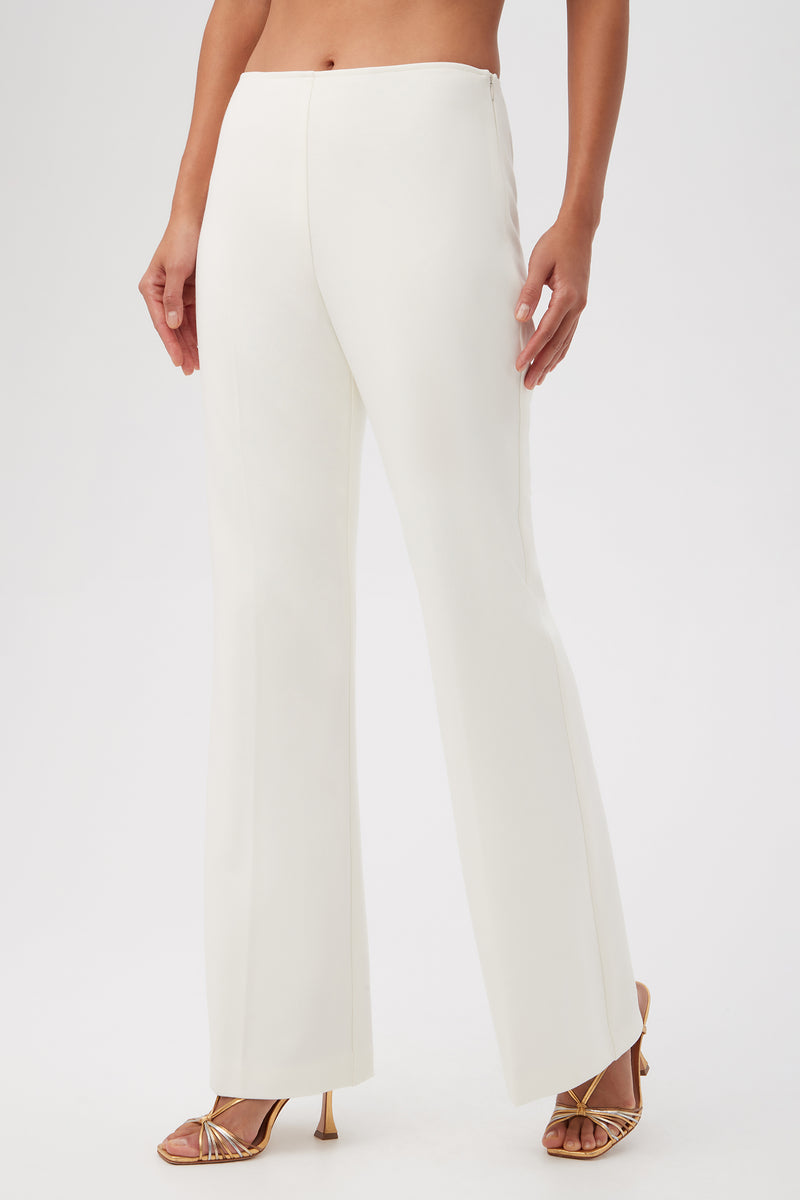 A person wears the Lancelot 2 Luxe Drape Bootcut Pants in high-waisted white, paired with gold strappy heels, standing against a plain white background. Photo is cropped at the chest.