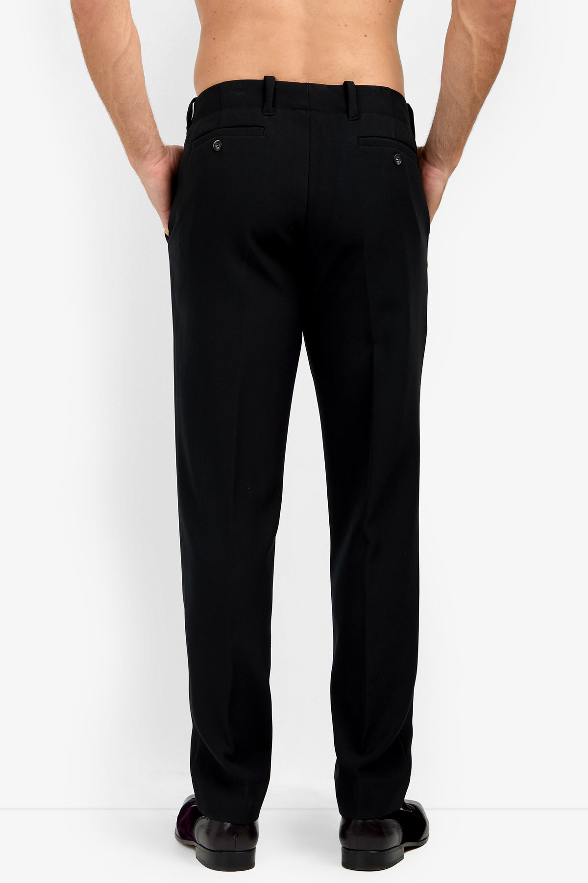 A man is seen from behind wearing the Alex Slim Trouser - Luxe Drape in black with matching shoes, hands in his back pockets, against a plain white background.