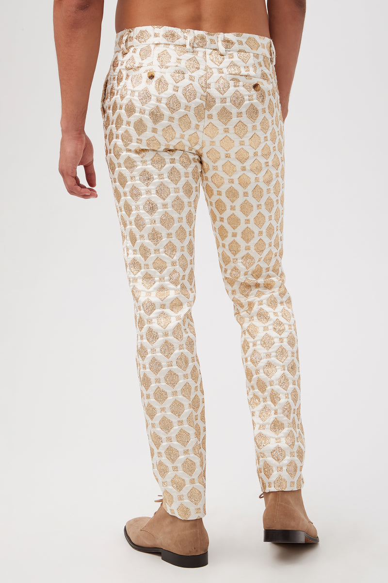A person, seen from behind, models the Clyde Slim Trouser - Jubilant JacquardÃ¢â‚¬â€cream pants with a gold geometric patternÃ¢â‚¬â€paired with brown shoes, shirtless, against a plain white background.
