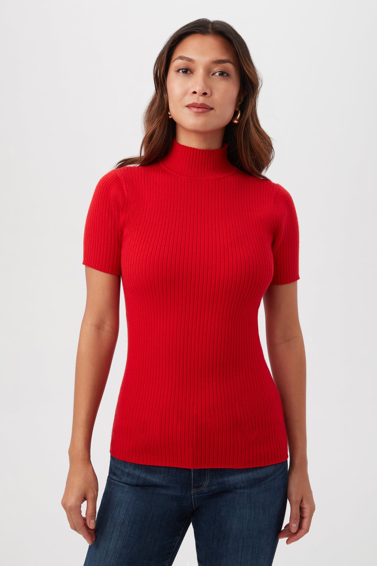 A woman stands facing forward, wearing the Armeni Merino Wool Short Sleeve Mockneck Top in bright red and dark blue jeans against a plain white background.