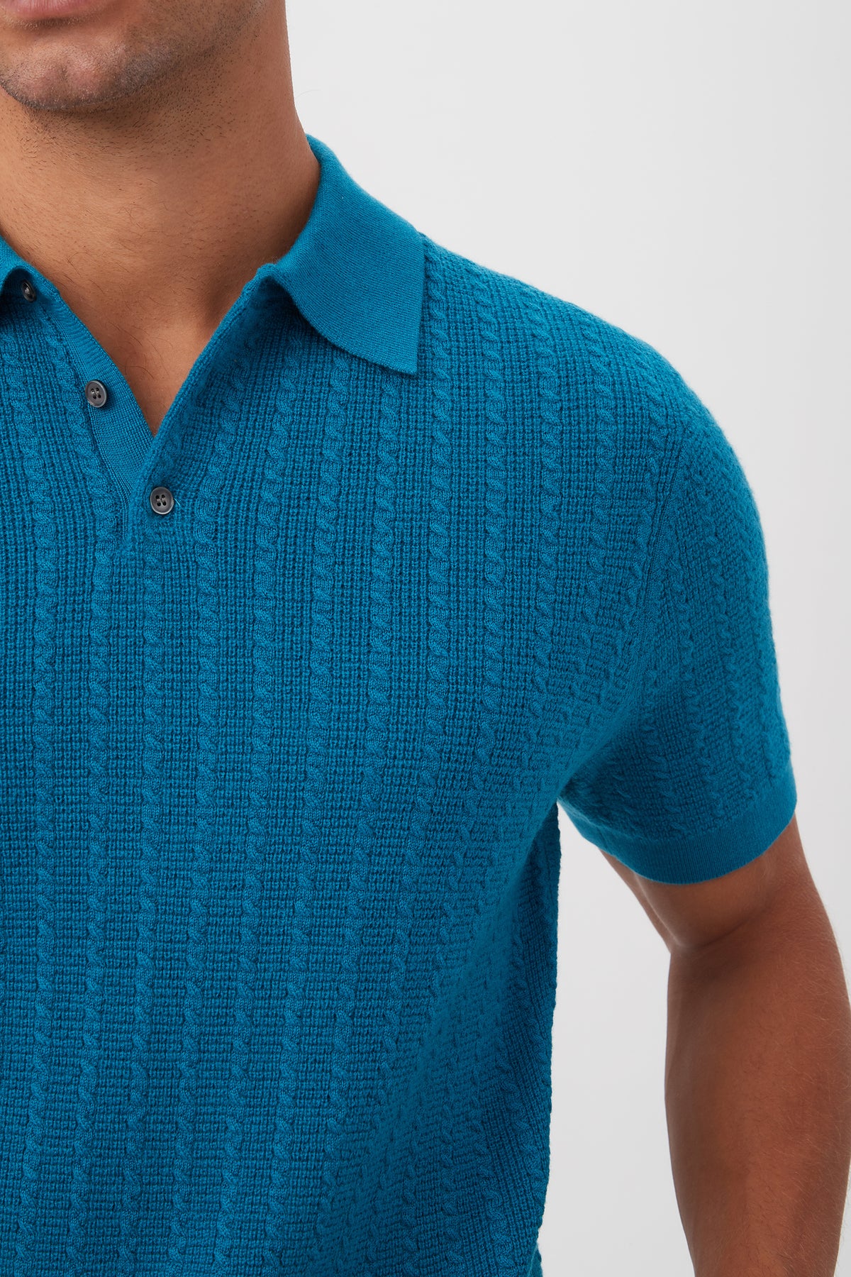 A person models the Asher Short-Sleeve Polo - Merino Wool in textured bright blue, featuring a collar and buttons, shown from shoulders to mid-torso against a plain light background.