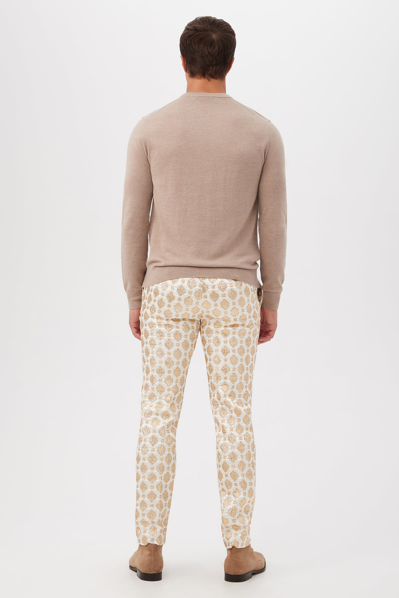 A man faces away against a plain white background, wearing the Weston Airedale Terrier Sweater in light beige merino wool, paired with patterned white and beige pants and tan shoes.