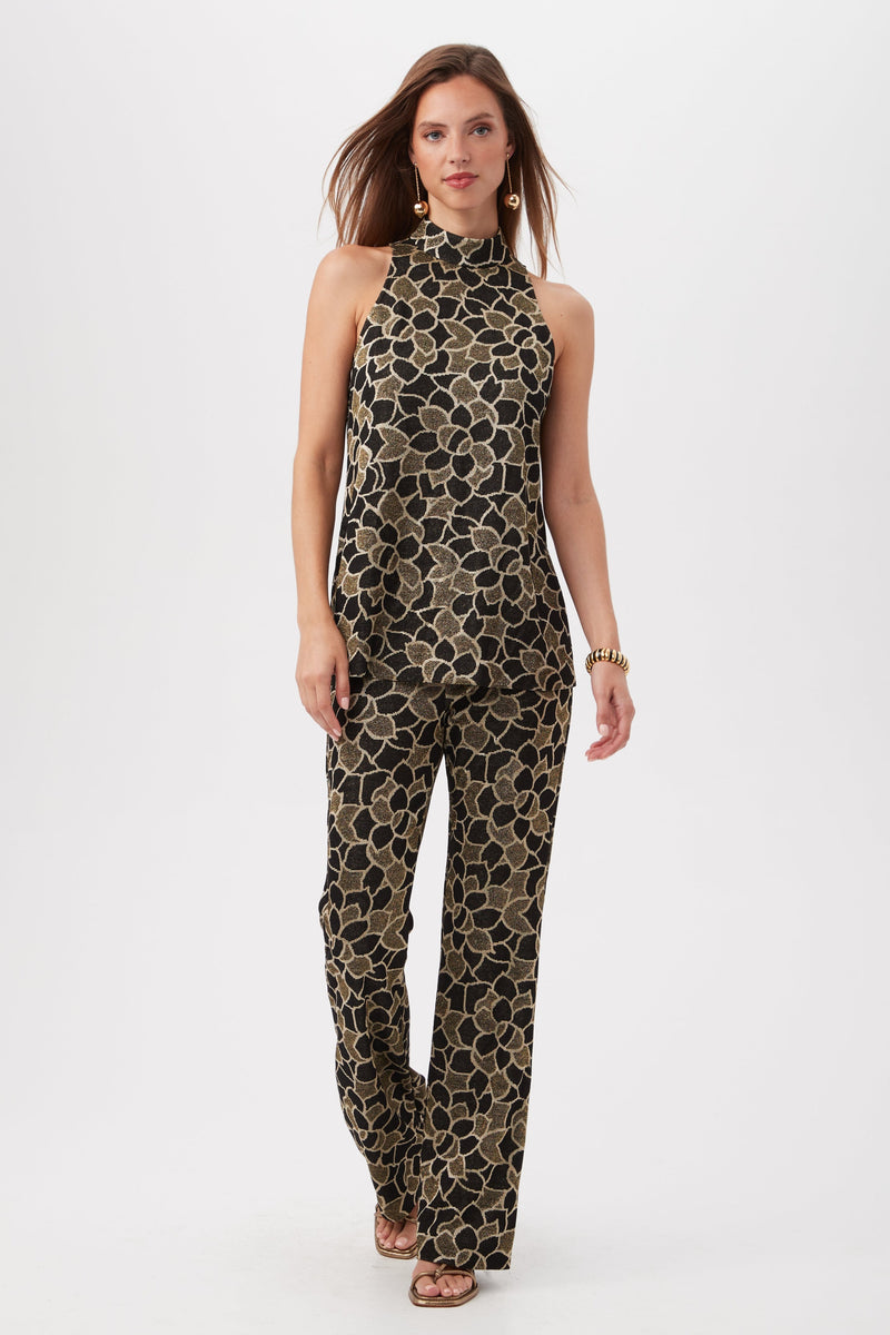 A woman walks confidently against a plain white background wearing Jacoba Metallic Knit Jacquard Bootcut Pants, gold earrings, a gold bracelet, and strappy heels.