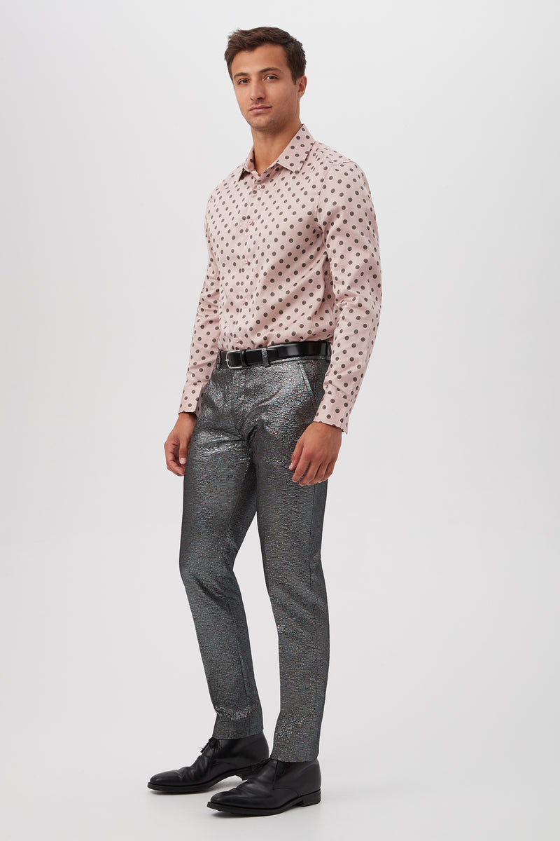 A man stands against a plain white background wearing the Aaron Slim Fit Long-Sleeve Shirt in light pink with dark polka dots, metallic silver textured pants, a black belt, and black dress shoes.