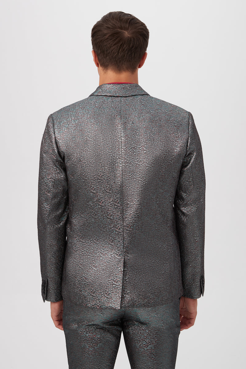 A person stands facing away from the camera wearing the Thurston Blazer in Mini Stained Glass Jacquard, a shiny, textured silver suit, against a plain white background.