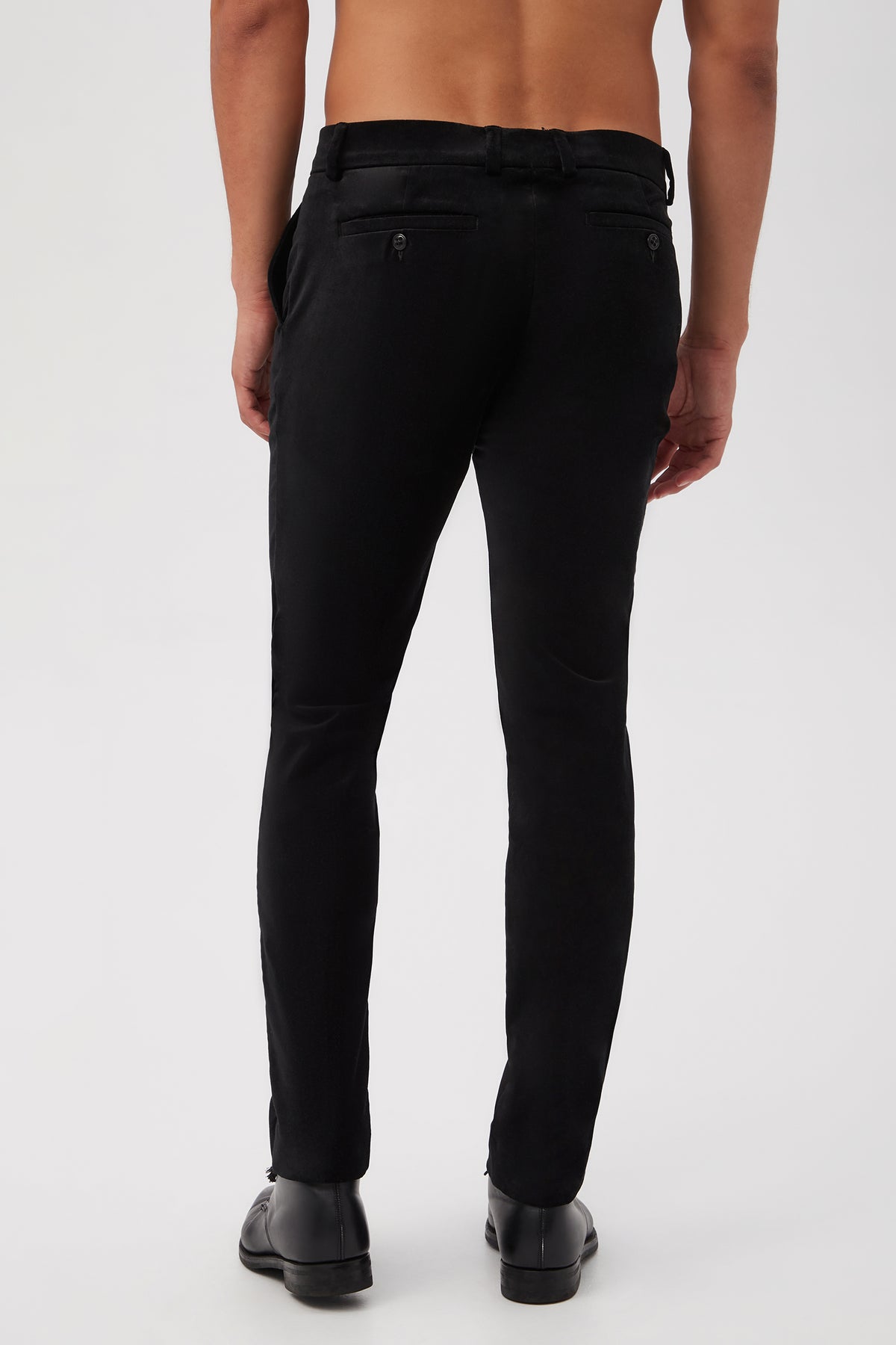 A shirtless person is shown from behind, wearing the Clyde Slim Trouser in Black Velveteen and black dress shoes against a plain white background.