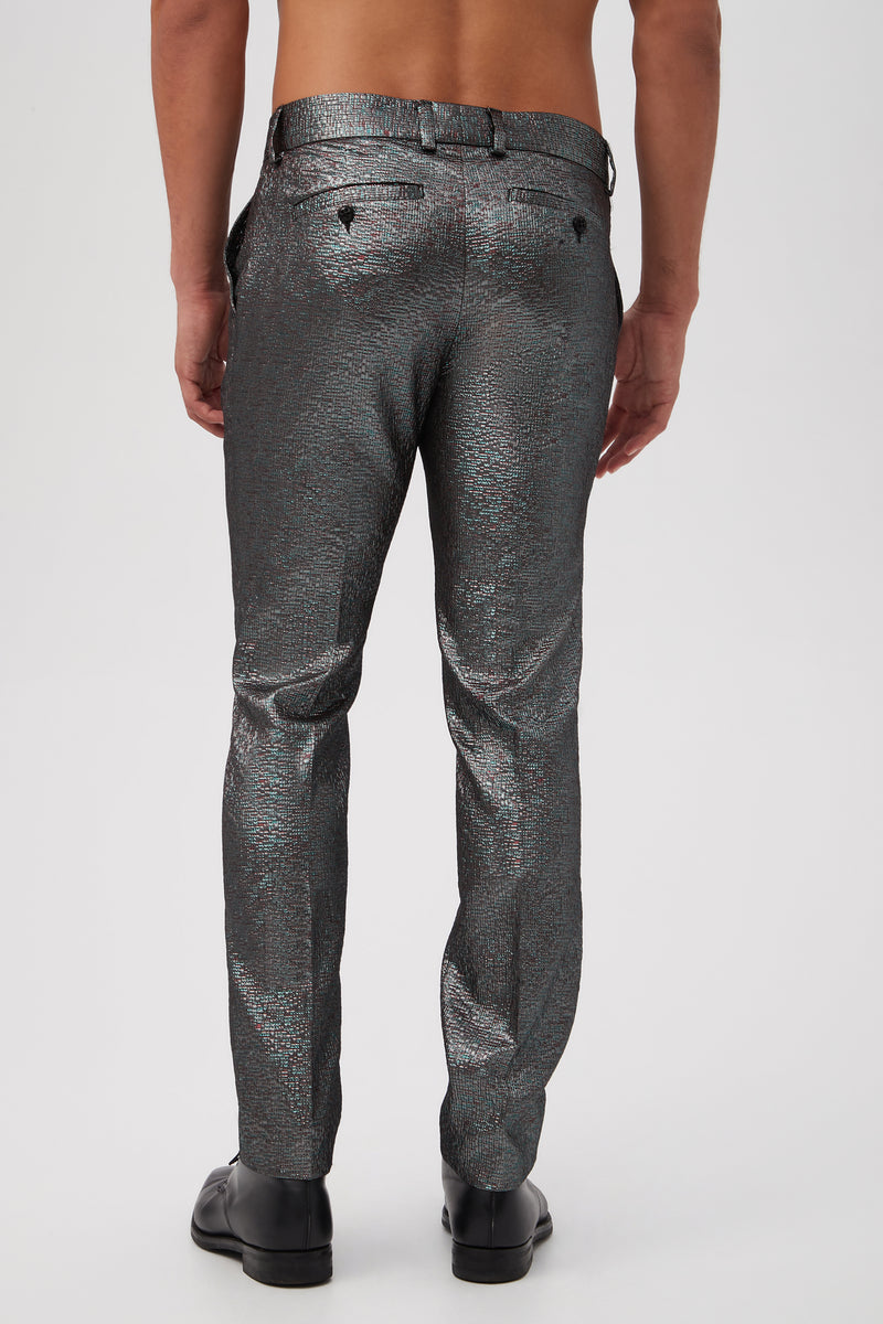 A shirtless man faces away, wearing Clyde Slim Trouser - Stained Glass Jacquard in shiny, textured silver and black dress shoes against a plain white background.