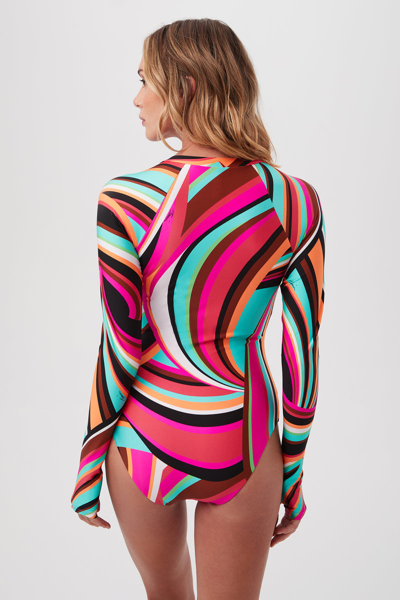 A woman with wavy blonde hair models the Swoop Long-Sleeve One-Piece Swimsuit, featuring a multicolored abstract pattern and adjustable lace-up front, as she stands with her back to the camera against a plain white background.