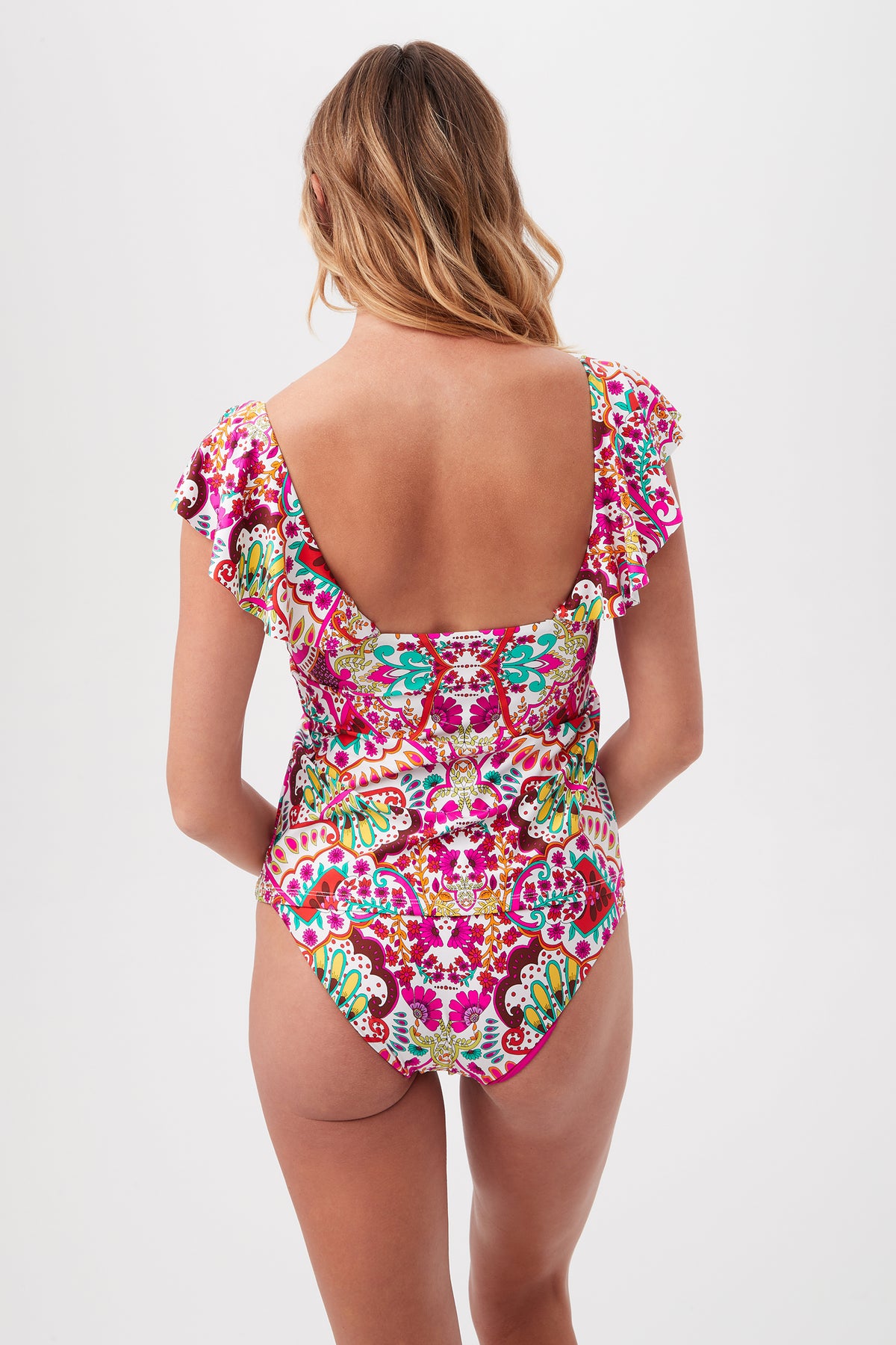 A woman with wavy hair is shown from the back wearing the Hawaiian Garden Ruffle V-Neck Tankini Swim Top, featuring colorful patterned fabric and ruffled sleeves, against a plain white background.