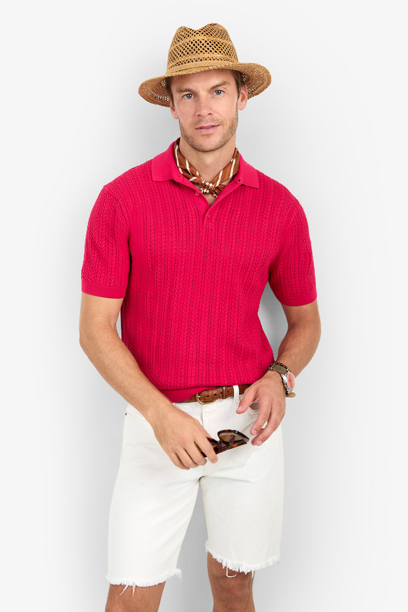 Man wearing a straw hat, Maxton Short-Sleeve Polo - Cotton Modal in red, white frayed shorts, brown belt, patterned neck scarf, and holding sunglasses against a plain light background.