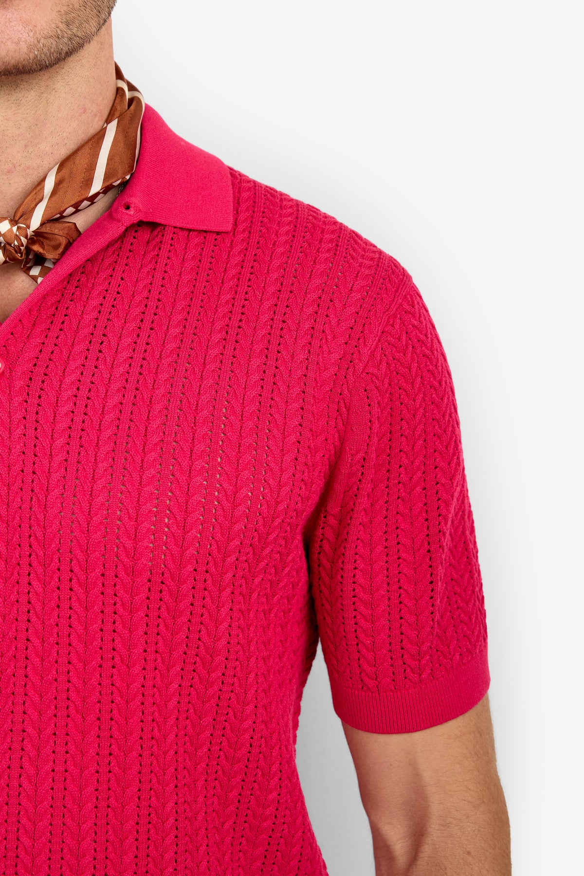 A person wearing the Maxton Short-Sleeve Polo - Cotton Modal in bright pink with a brown patterned scarf, shown from the shoulders up against a white background.