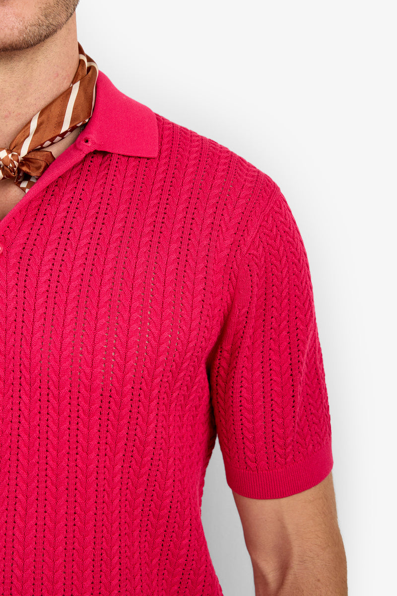 A person wearing the Maxton Short-Sleeve Polo - Cotton Modal in bright pink with a brown patterned scarf, shown from the shoulders up against a white background.