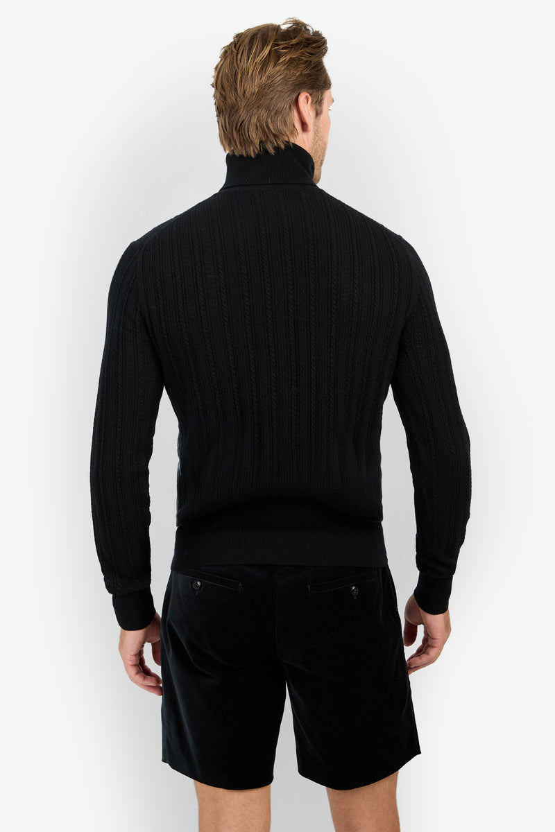 A man with light brown hair stands facing away in a black Oberon Turtleneck Sweater - Merino Wool and black shorts, arms relaxed by his sides against a plain white background.