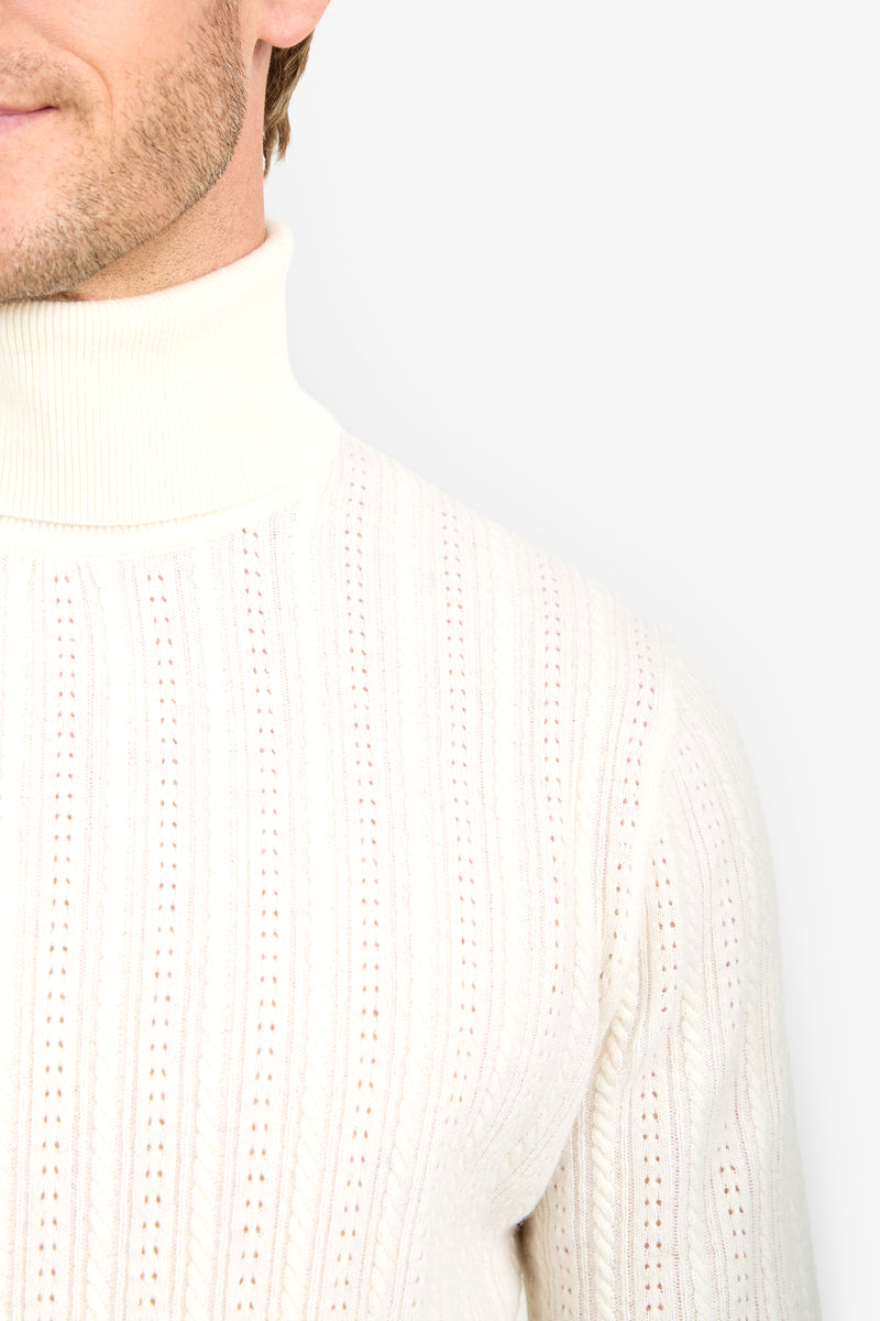 A close-up of a person wearing the Oberon Turtleneck Sweater - Merino Wool in cream, showing part of their face and upper chest against a plain light background.