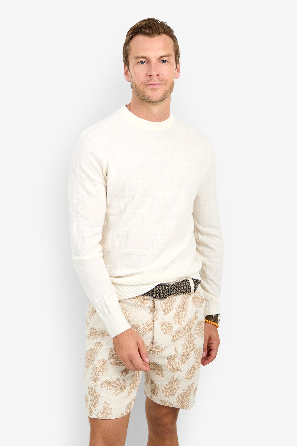 A man wears the Mr Turk Crewneck Sweater - Merino Wool and beige leaf-patterned shorts, standing against a plain light background and looking at the camera with a neutral expression.
