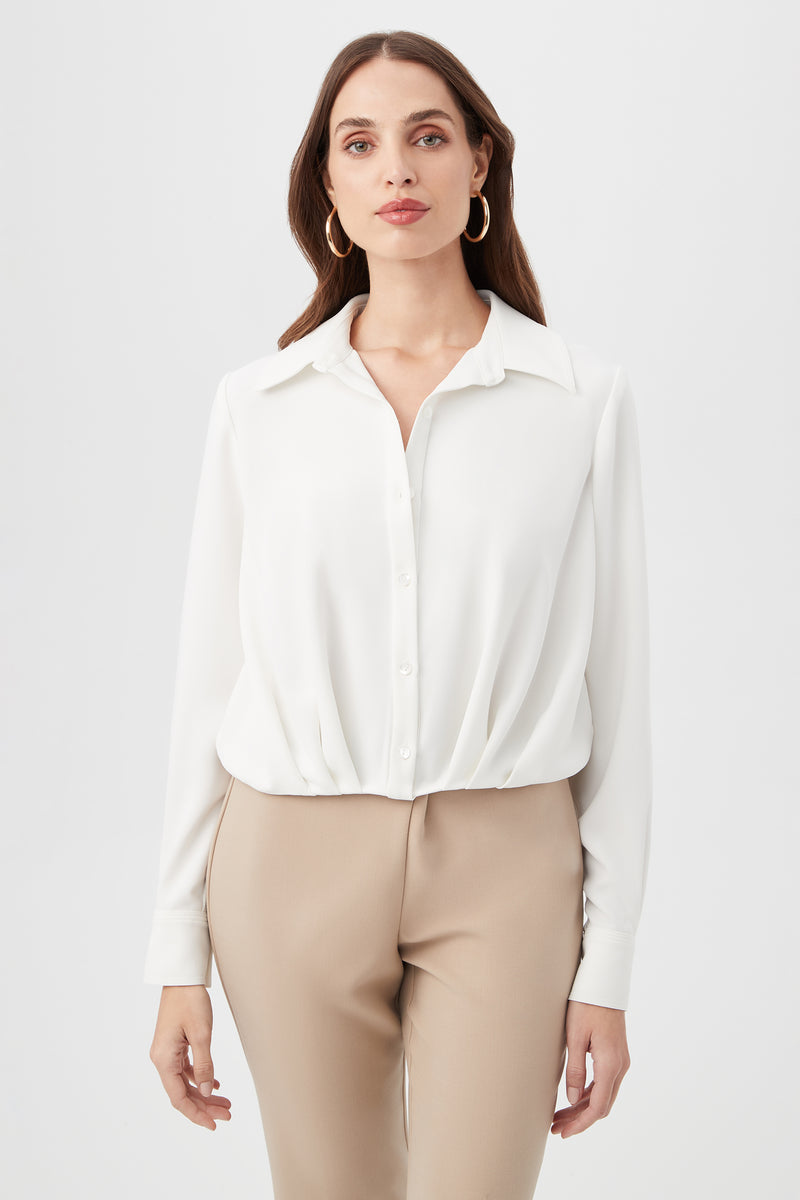 A woman with long brown hair wears gold hoop earrings, beige pants, and the Renlee Shirt—a white collared button-up—while standing against a plain white background and looking at the camera.