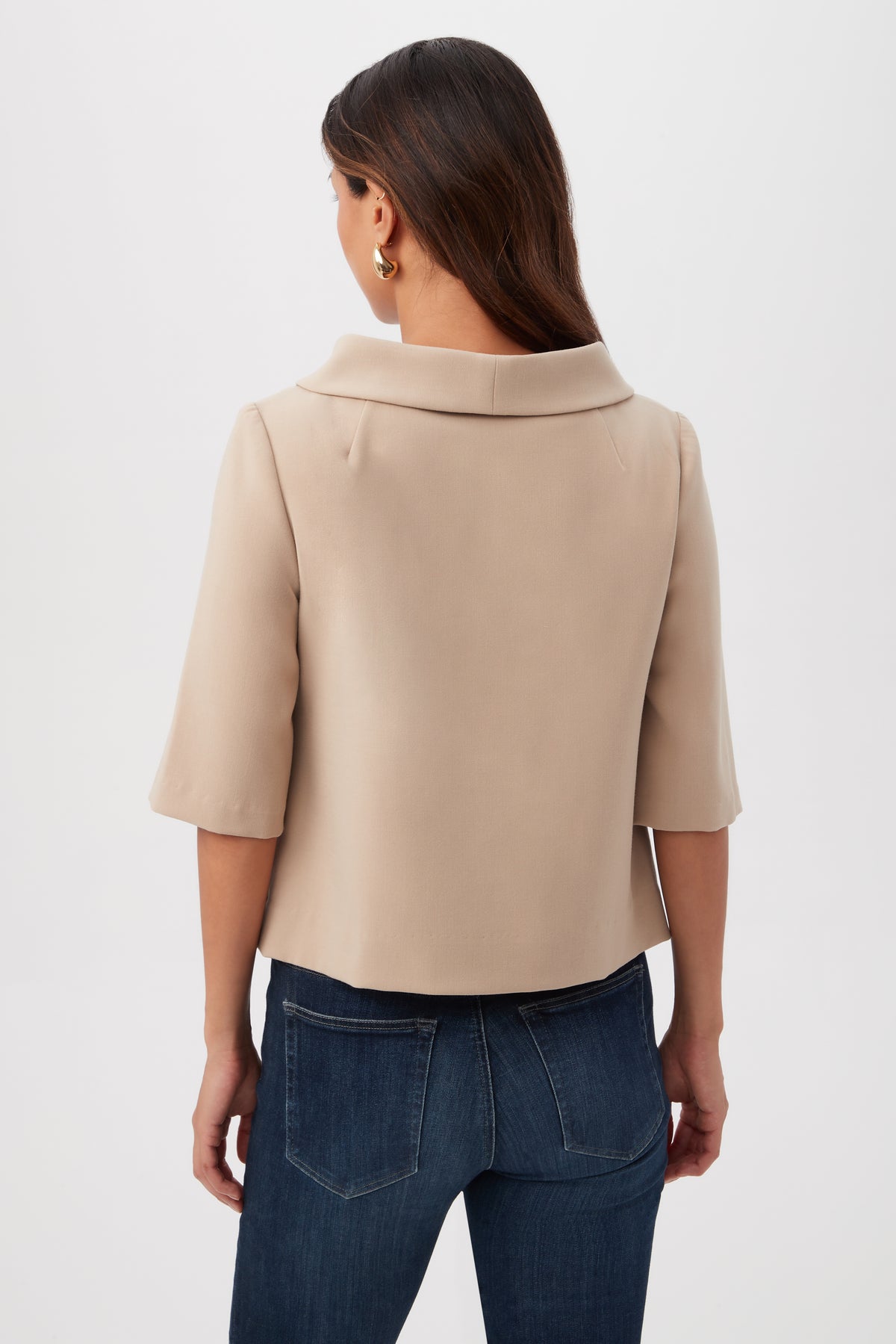 A woman with long brown hair is seen from the back wearing the Kailee Short-Sleeve Folded Collar Top in beige and dark blue jeans, against a plain white background.