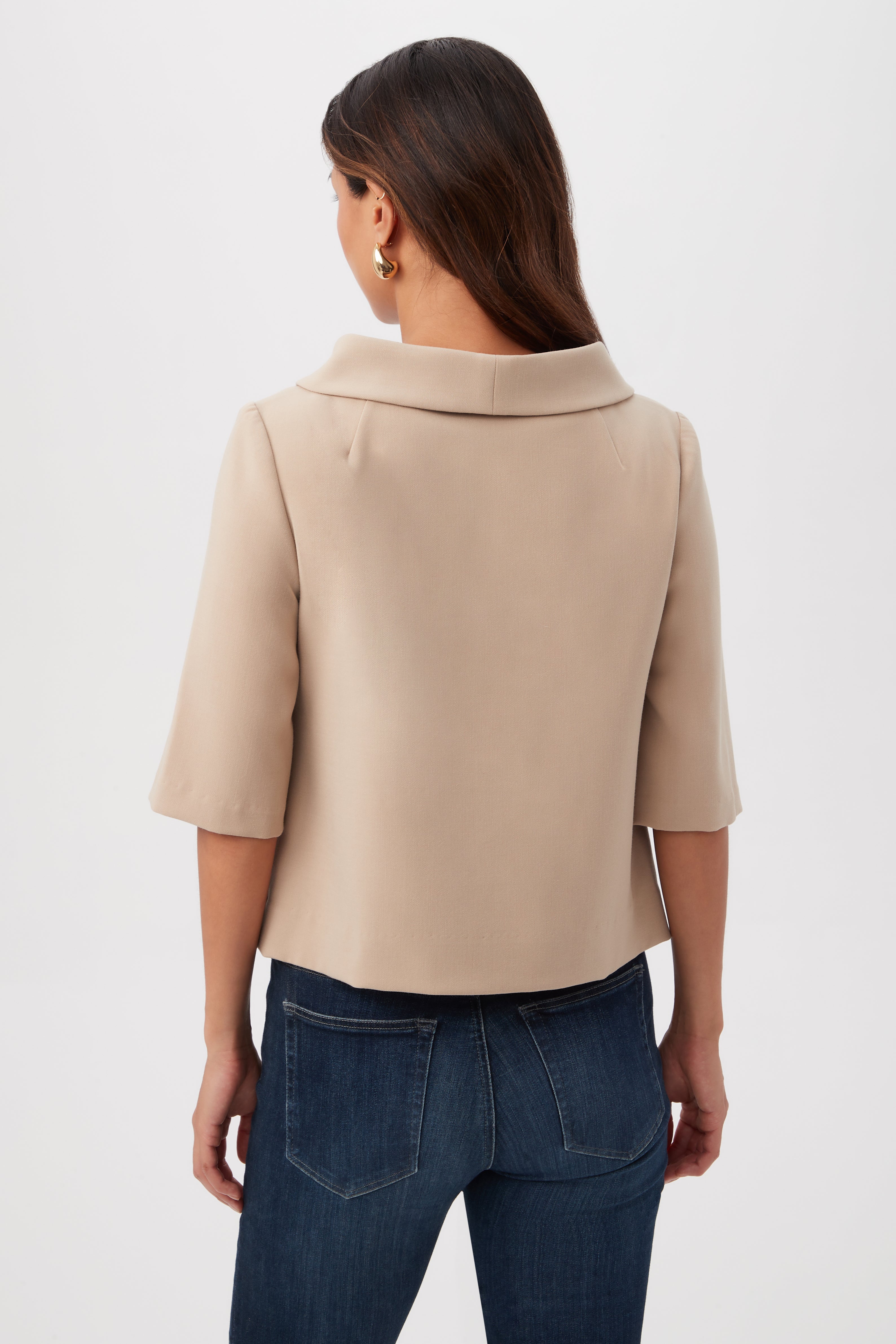 A woman with long brown hair is seen from the back wearing the Kailee Short-Sleeve Folded Collar Top in beige and dark blue jeans, against a plain white background.