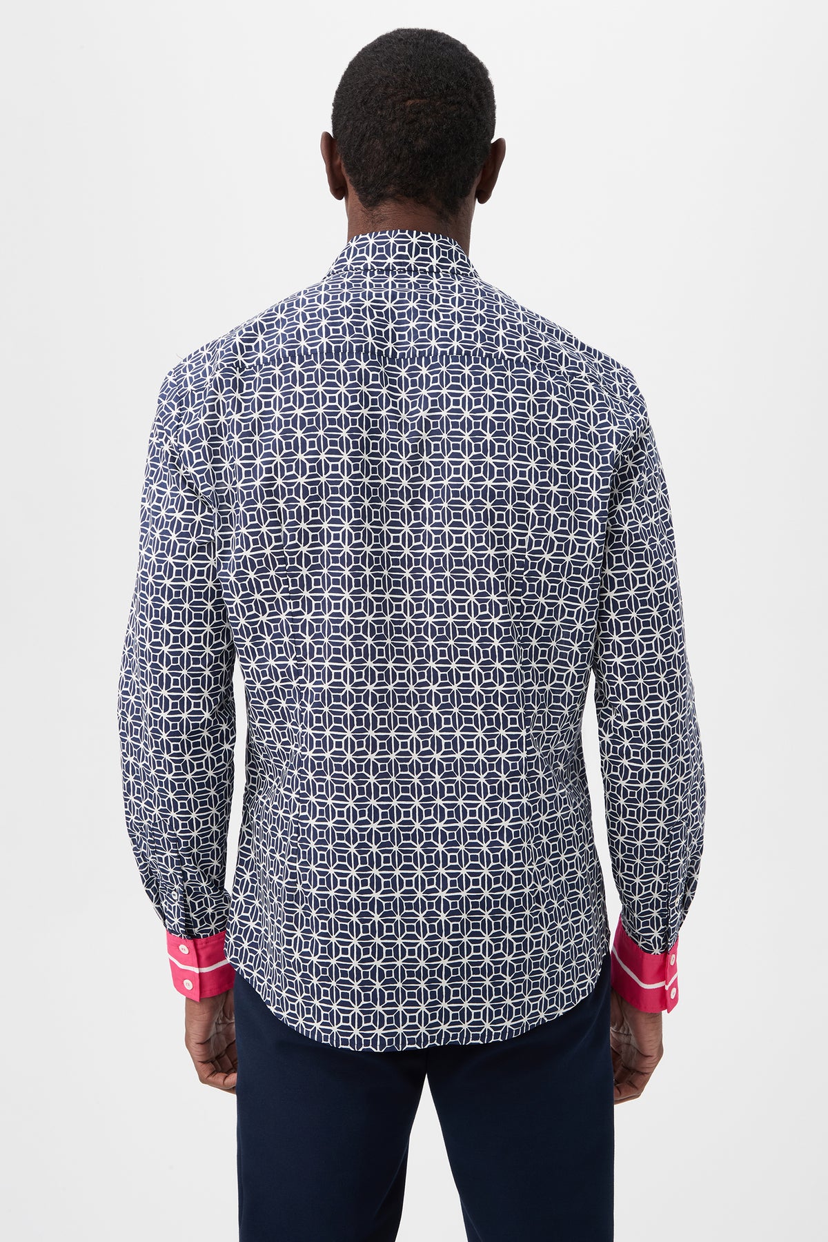 A man stands facing away, wearing the Aaron 2 Slim Long-Sleeve Shirt in navy blue and white with bright pink cuffs and dark pants, set against a plain white background.
