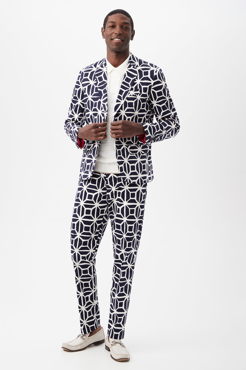 A man smiles in the Clyde Slim Trouser - Durell Herringbone, paired with a matching jacket, white shirt, and white loafers, set against a plain white background.