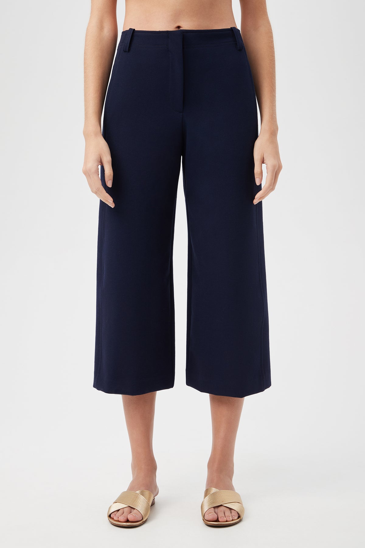 Model wears the Patyn Pant in indigo with light sandals, standing against a white background. The image is cropped at the chest and feet.