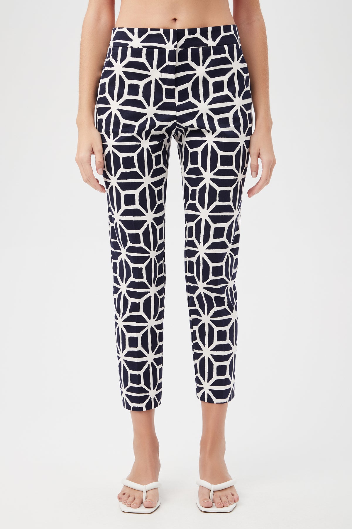 A person wearing the Moss 2 Slim Crop Pant - Durell Herringbone in indigo, featuring a high waist and ankle-length cut with a bold geometric pattern, paired with white sandals. The image is cropped from the shoulders down.