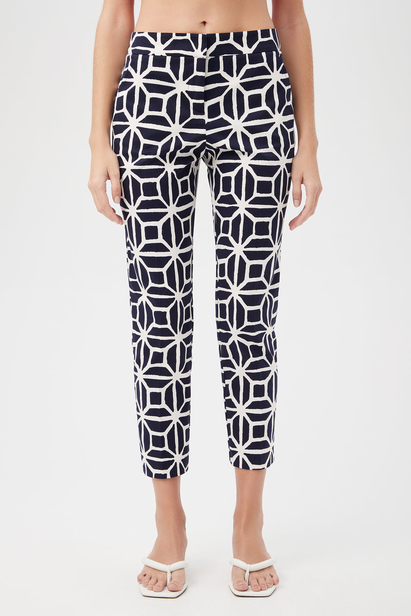 A person wearing the Moss 2 Slim Crop Pant - Durell Herringbone in indigo, featuring a high waist and ankle-length cut with a bold geometric pattern, paired with white sandals. The image is cropped from the shoulders down.