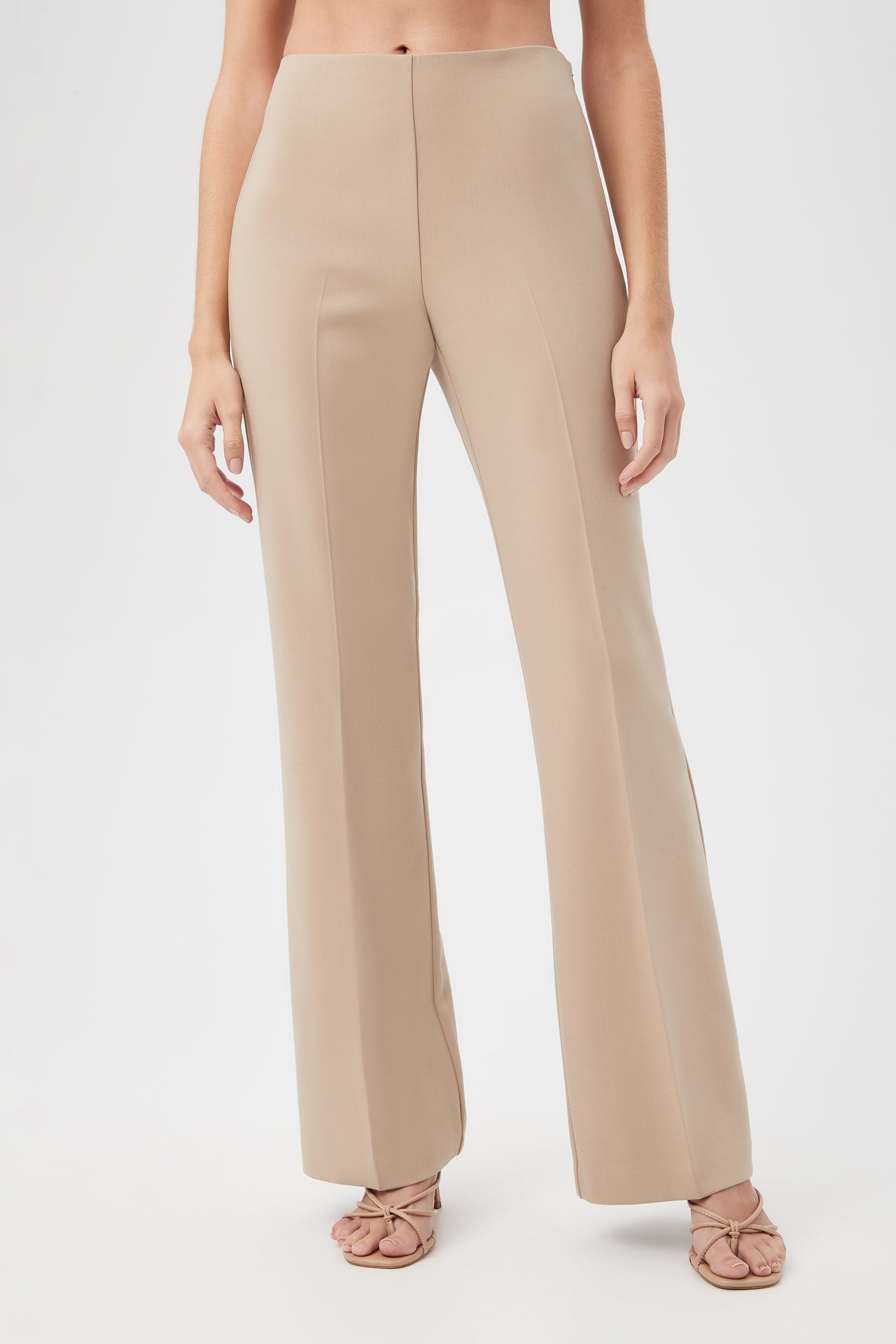 A woman wearing Jacoba Slim-Fit Stretch Bootcut Pants in Beach and strappy nude heels stands against a plain white background, with her upper body mostly out of frame.