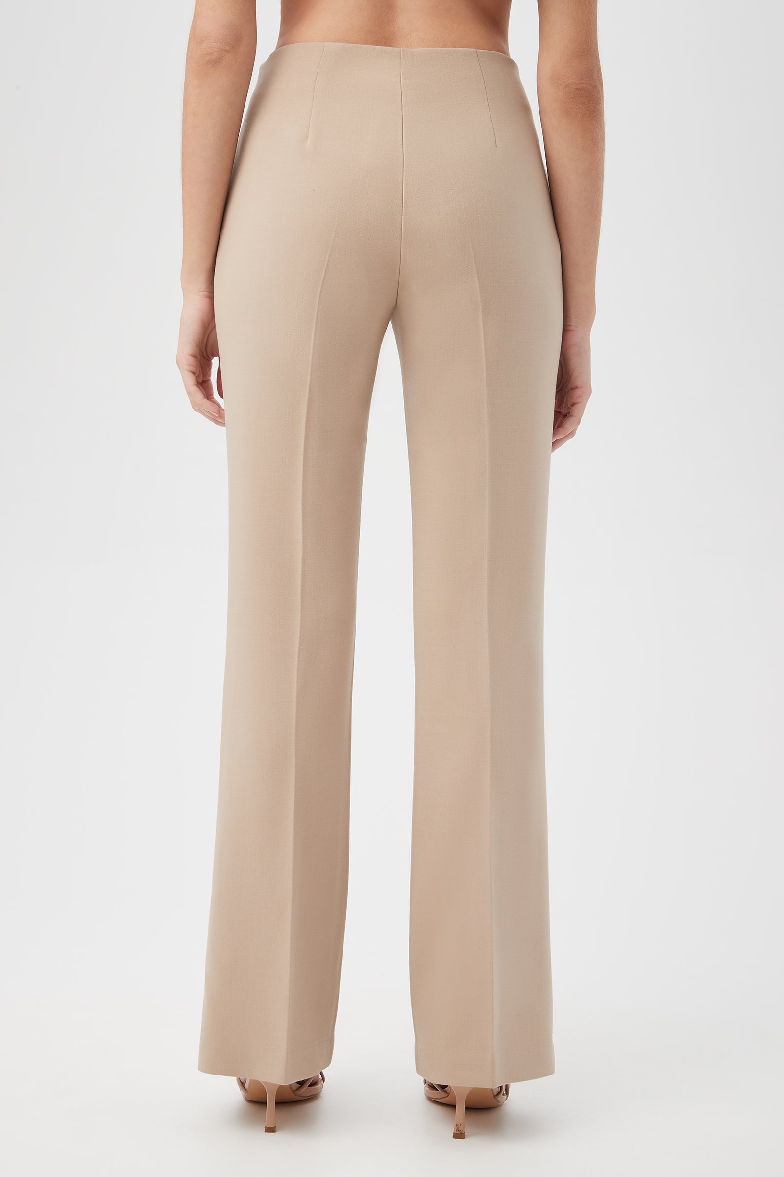 A person wearing Jacoba Slim-Fit Stretch Bootcut Pants in beige and beige heeled sandals, shown from the back against a plain white background.