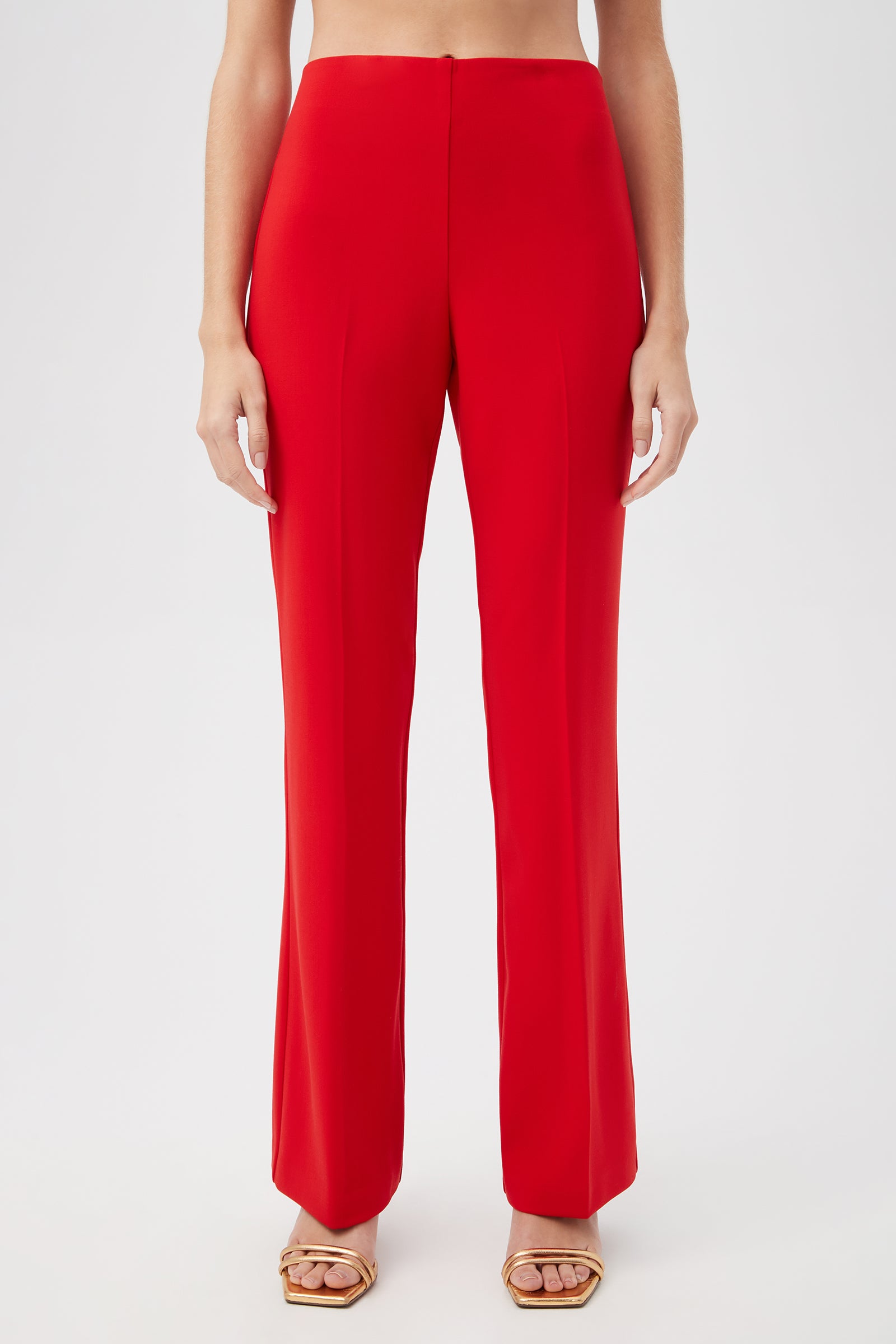 A person shown from the waist down against a plain light background wears Jacoba Slim-Fit Stretch Bootcut Pants in bright red with gold open-toe heels.