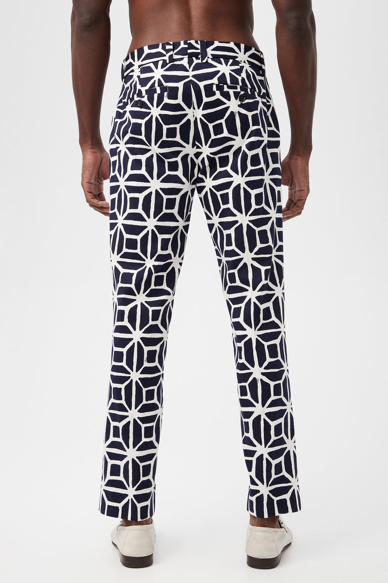 A man faces away, wearing the Clyde Slim Trouser in Durell Herringbone with a navy and white geometric pattern and light shoes, set against a plain white background.