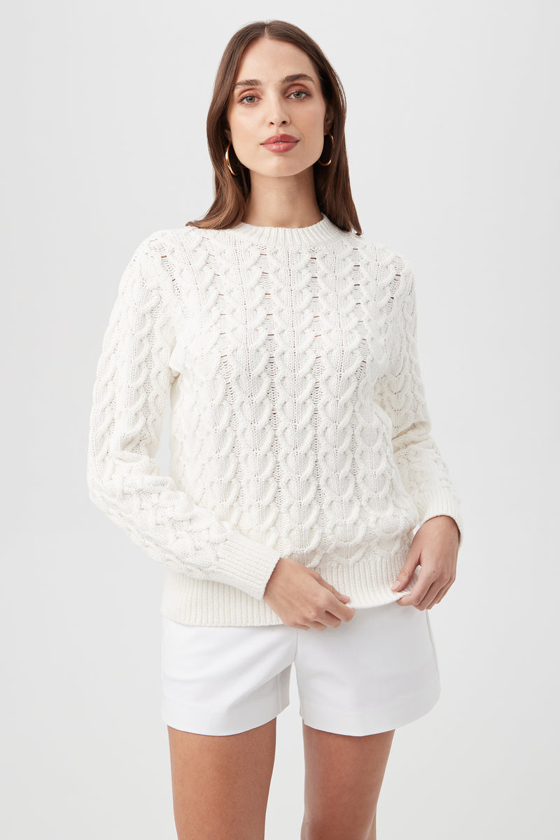 Model wears the Corazon Heart Knit Crewneck Sweater in Whitewash with white shorts, standing against a light background and looking forward with a neutral expression.