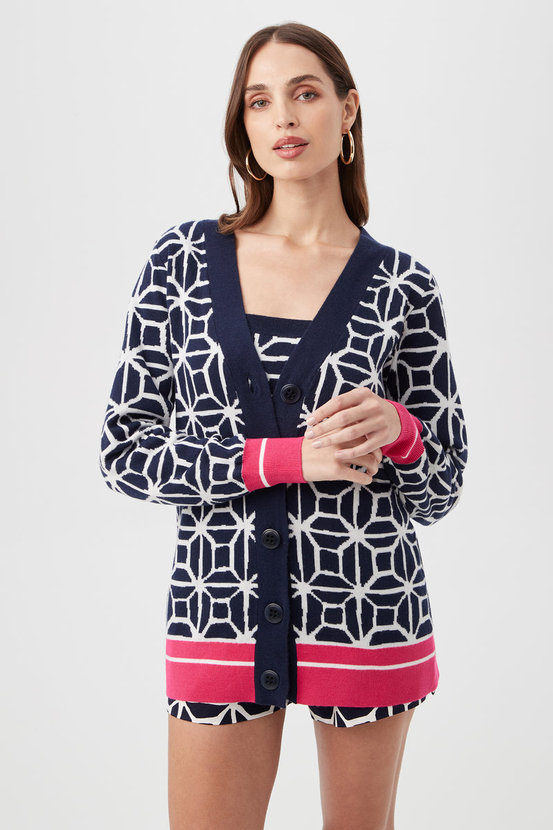 A woman with long brown hair and hoop earrings wears the South Bay V-Neck Cardigan - Durell Knit in Multi over a matching top, standing against a plain light background.