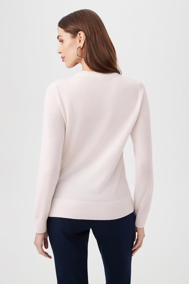 A woman with long brown hair wears the Love Merino Wool Crewneck Sweater in light pink and dark pants, standing with her back to the camera against a plain light background.