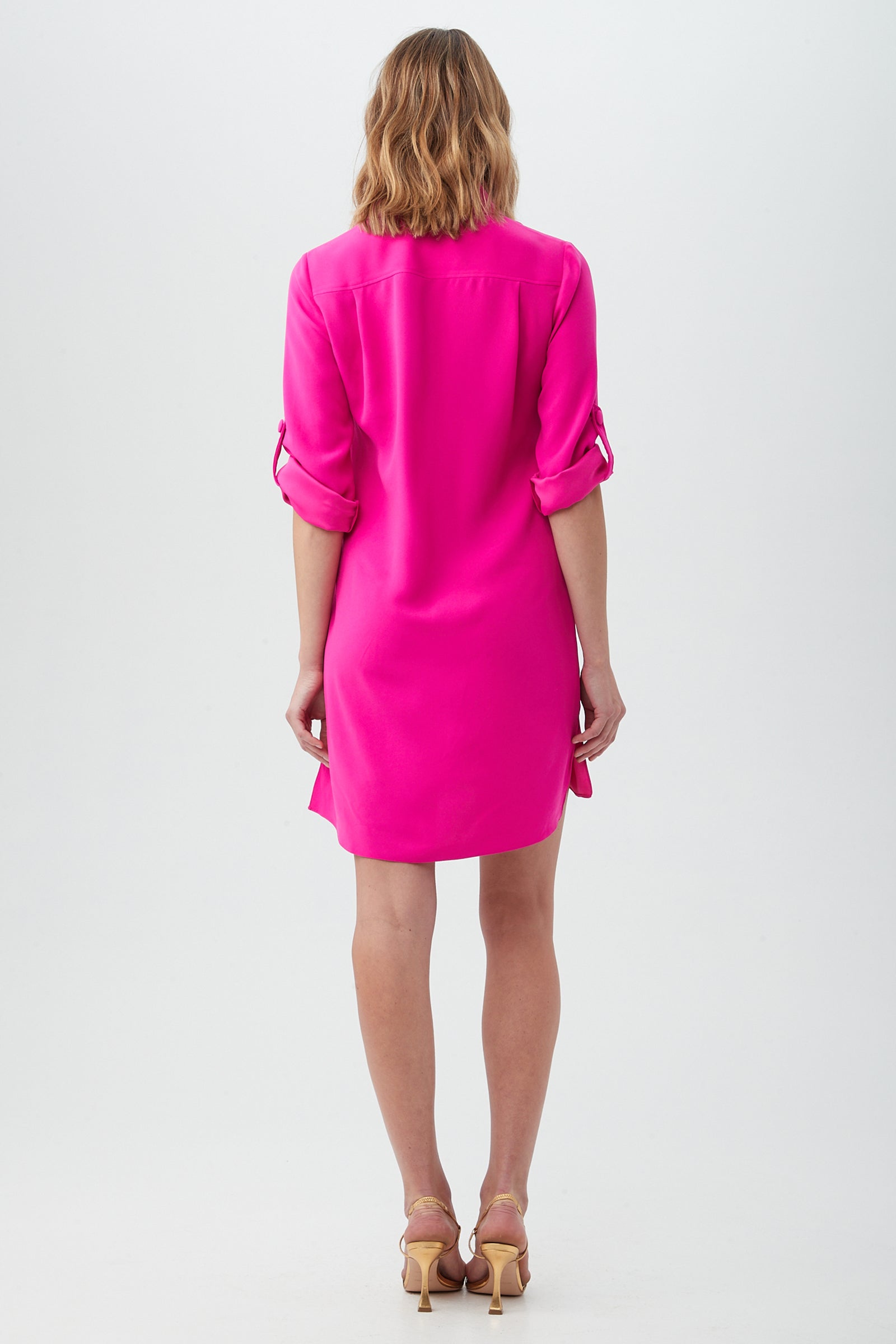 A person with shoulder-length blonde hair, seen from behind, models the Portrait Shirt Dress in bright pink with beige heeled sandals against a plain white background.