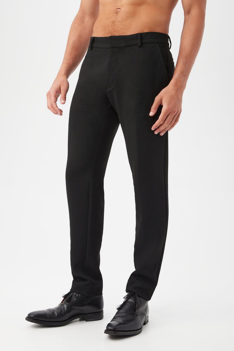 A person models the Clyde Slim Trouser - Hi-Line Suiting with black dress shoes, standing against a plain white background. The image emphasizes the lower half of the body to showcase the trousers fit and style.