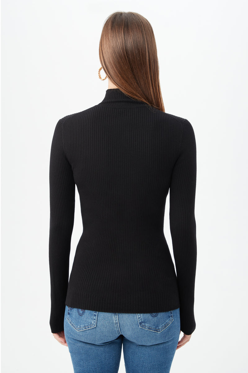 A woman with long brown hair, wearing the fitted black Hempstead Sweater and blue jeans, is shown from behind against a plain white background.